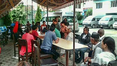 People sit at tables under an awning in a courtyard, with three white Deerwalk vans parked in a row behind them.