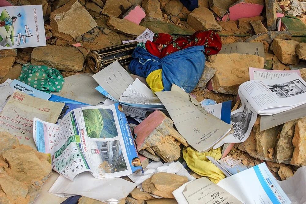 School exercise books, a wall calendar and children's clothes lie scattered and open among stone rubble.