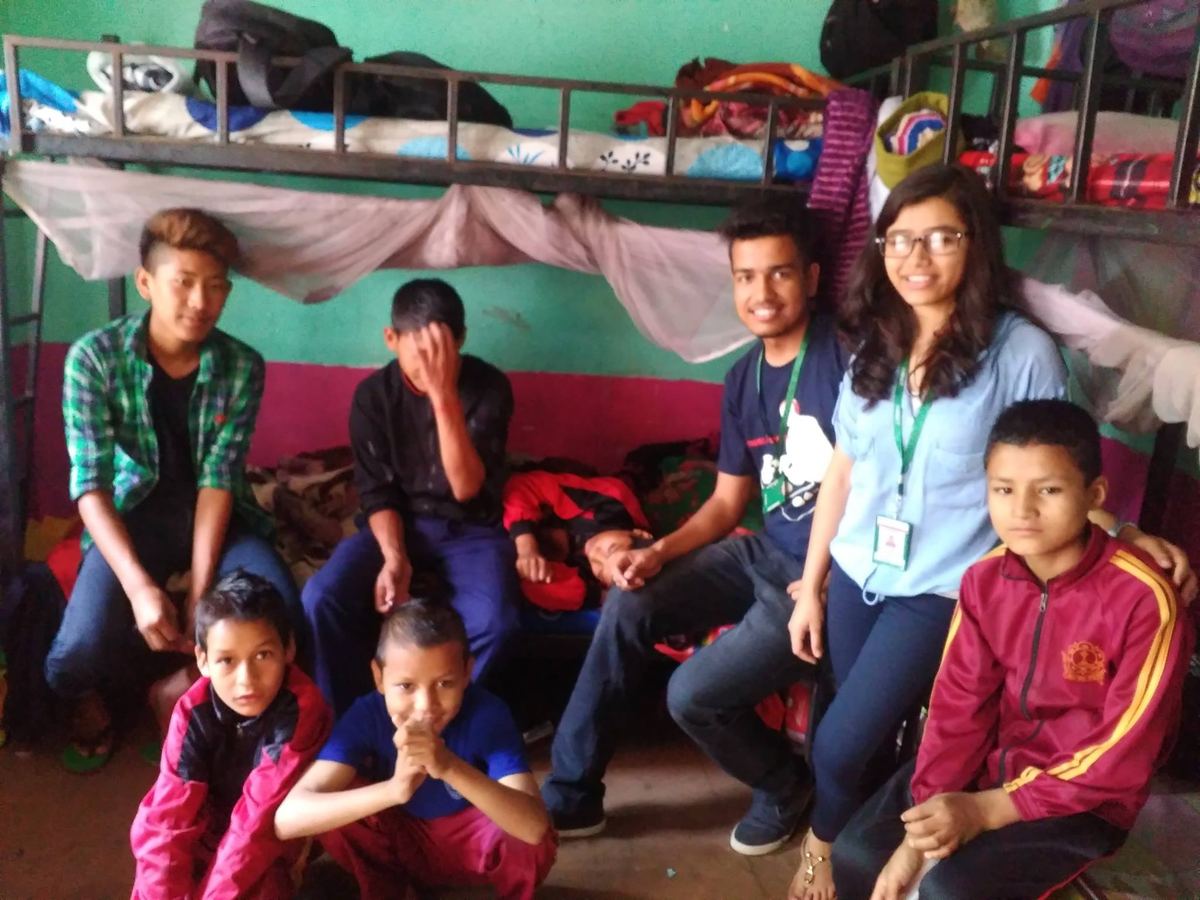 Two visitors and seven children pose together in front of the bunk beds, several of the children laughing.