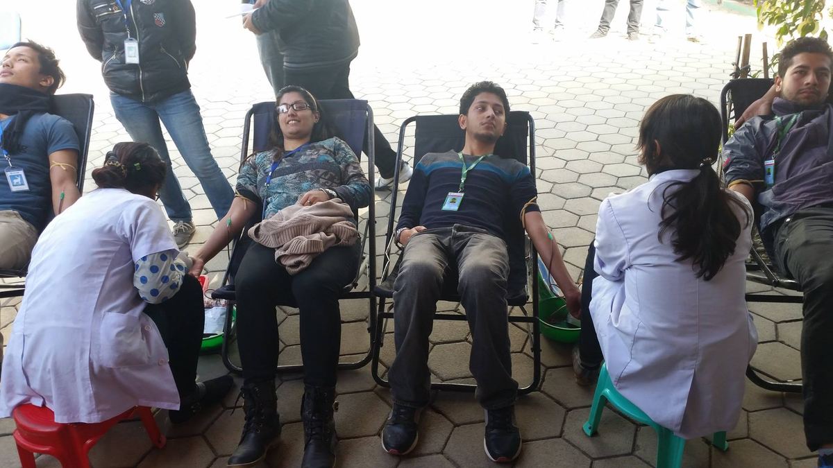 Two donors recline in camp chairs on the paving while nurses in white coats attend to them.