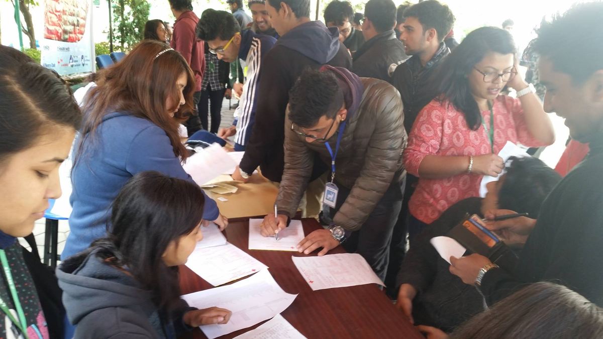 Students crowd around a registration table filling in forms, with staff seated on the far side.