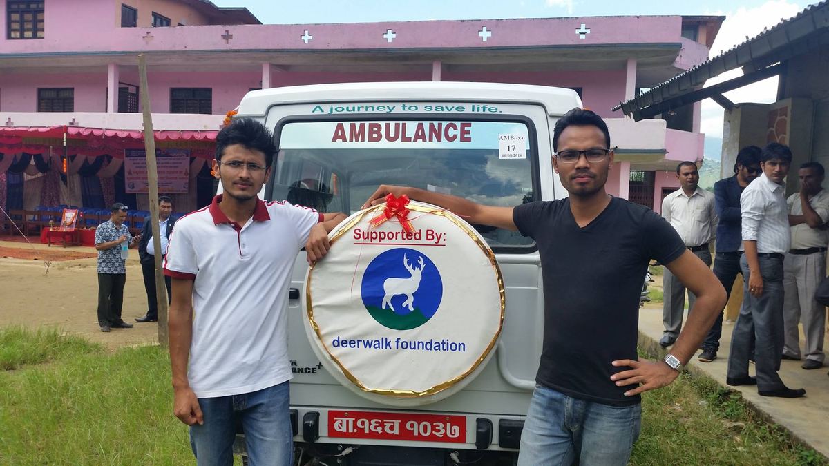 Two men stand at the front of the ambulance, one resting a hand on a round Supported By deerwalk foundation emblem on the bonnet.