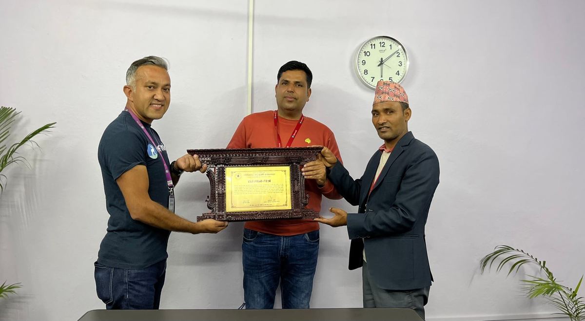 Three men hold a framed appreciation plaque between them in an office.