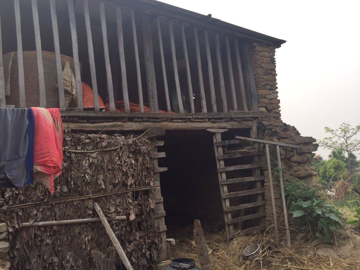 A timber and stone barn with an open ground floor, washing hung over a beam and firewood stacked inside.