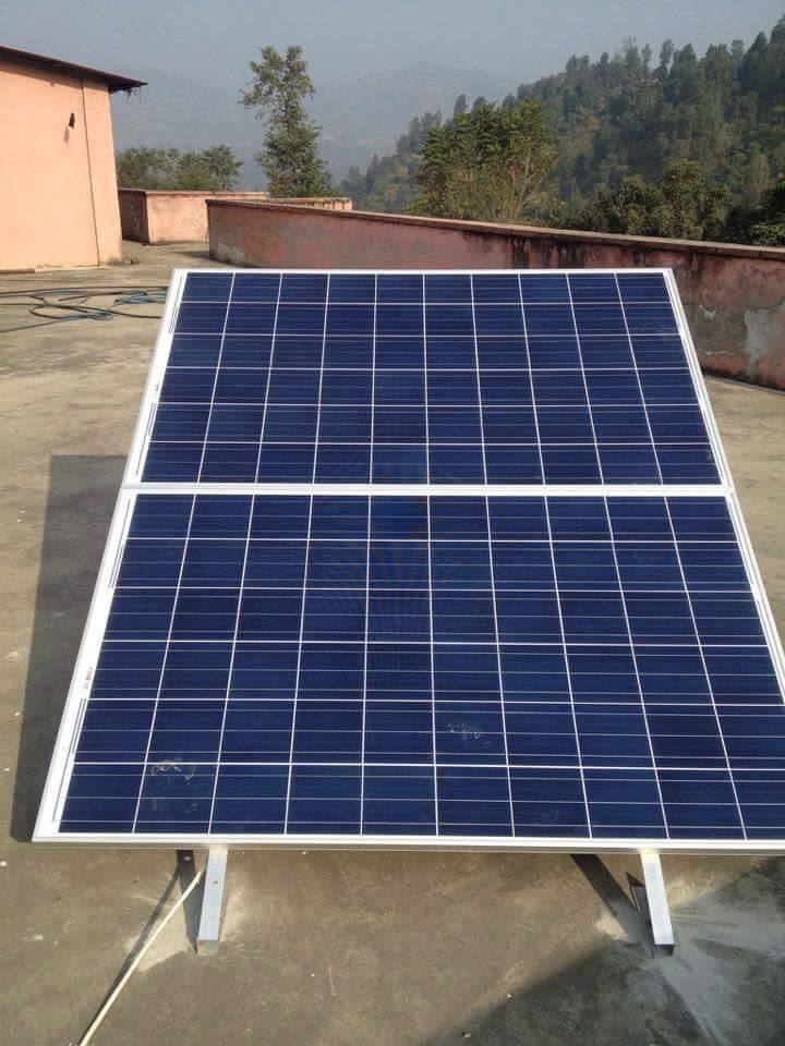 A solar panel mounted on a flat concrete roof, tilted towards the sky, with forested hills behind.