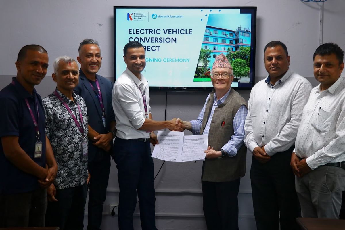 Representatives of Deerwalk Foundation and the National Innovation Centre shake hands over the signed agreement, with seven attendees standing before a screen reading Electric Vehicle Conversion Project, signing ceremony.