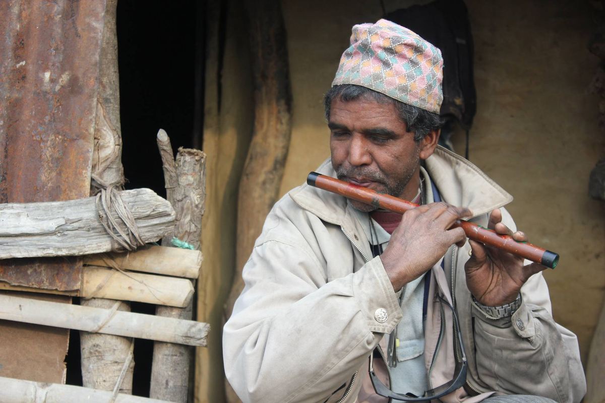 The same man raises a wooden flute to his lips, leaning against a timber railing.