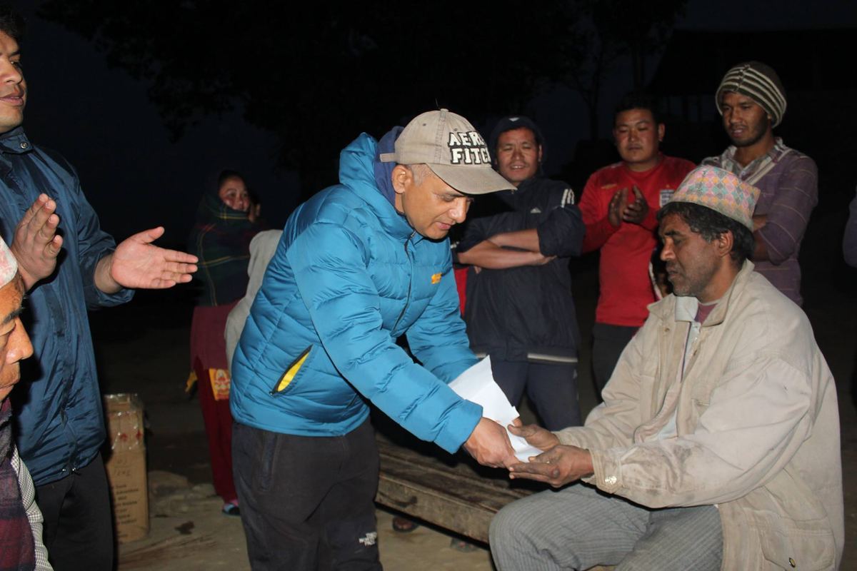 A man in a blue jacket leans in to place folded notes into the porter's hands, watched by a small crowd in the dark.
