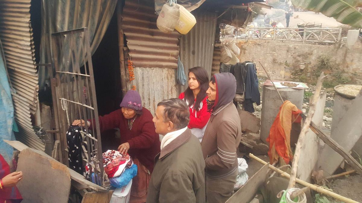 Visitors hand bundles of clothing to the woman and a neighbour outside a tin shelter hung with washing.