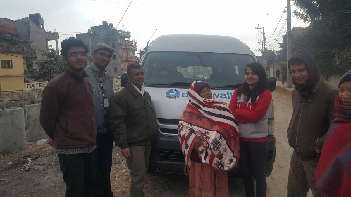 A group stands beside a white Deerwalk van on a lane, the woman in her new blanket among them.