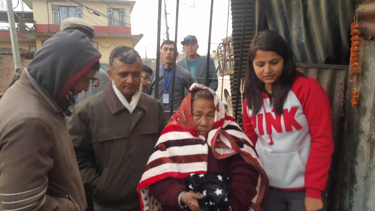 Visitors gather closely around the woman beside a metal gate, one holding her arm.