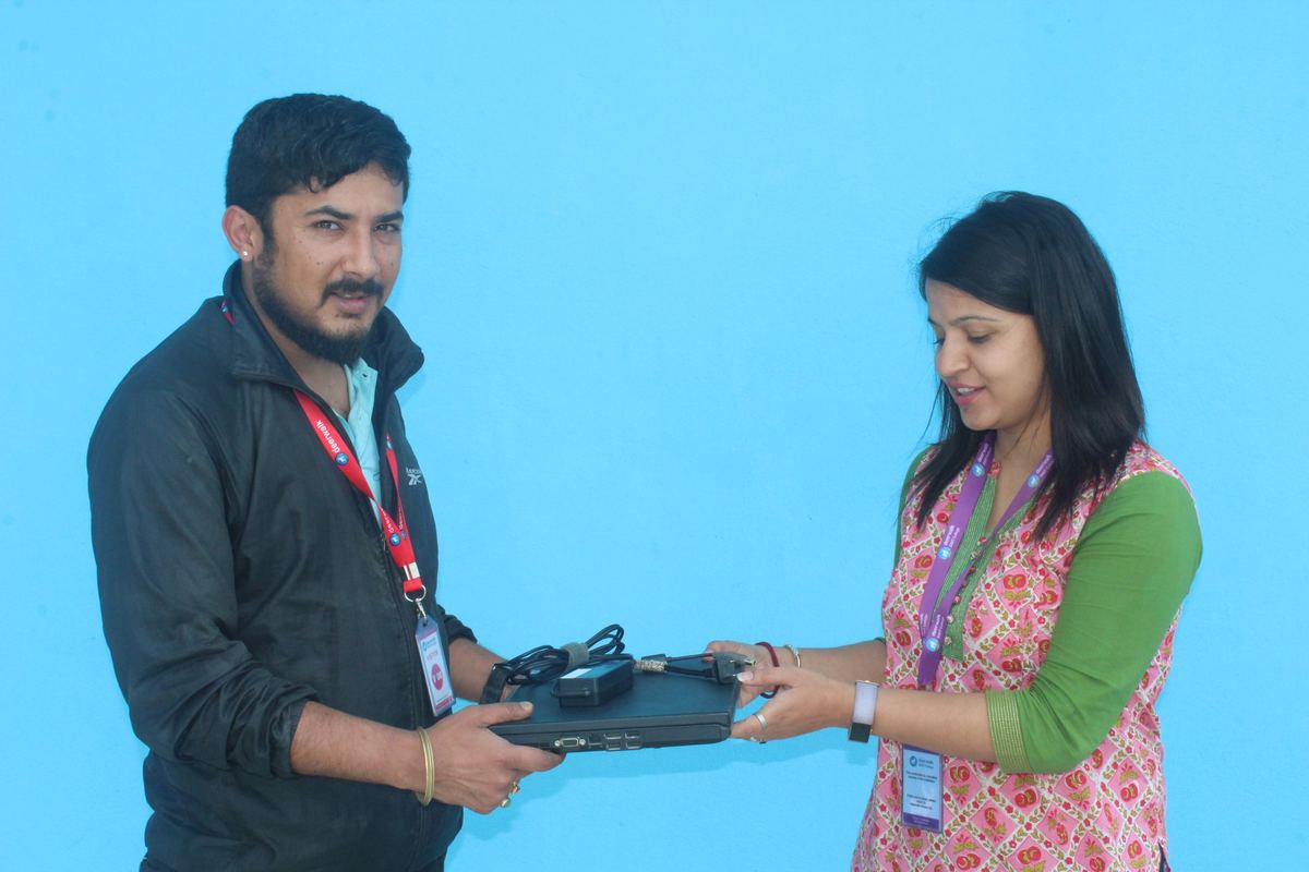 A man and a woman, both wearing lanyards, hold a laptop between them against a plain blue backdrop.