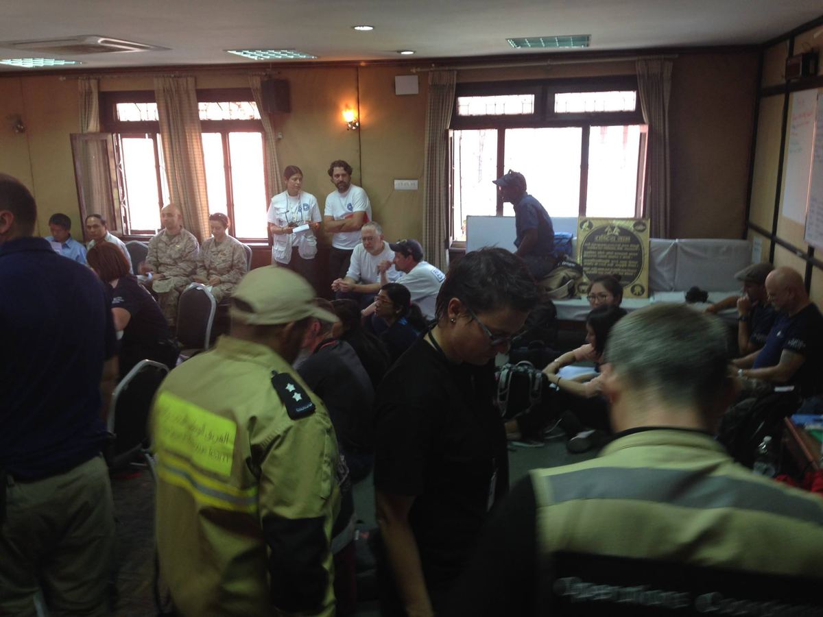 Delegates stand in a panelled meeting room, several in high visibility uniforms, facing the front of the hall.