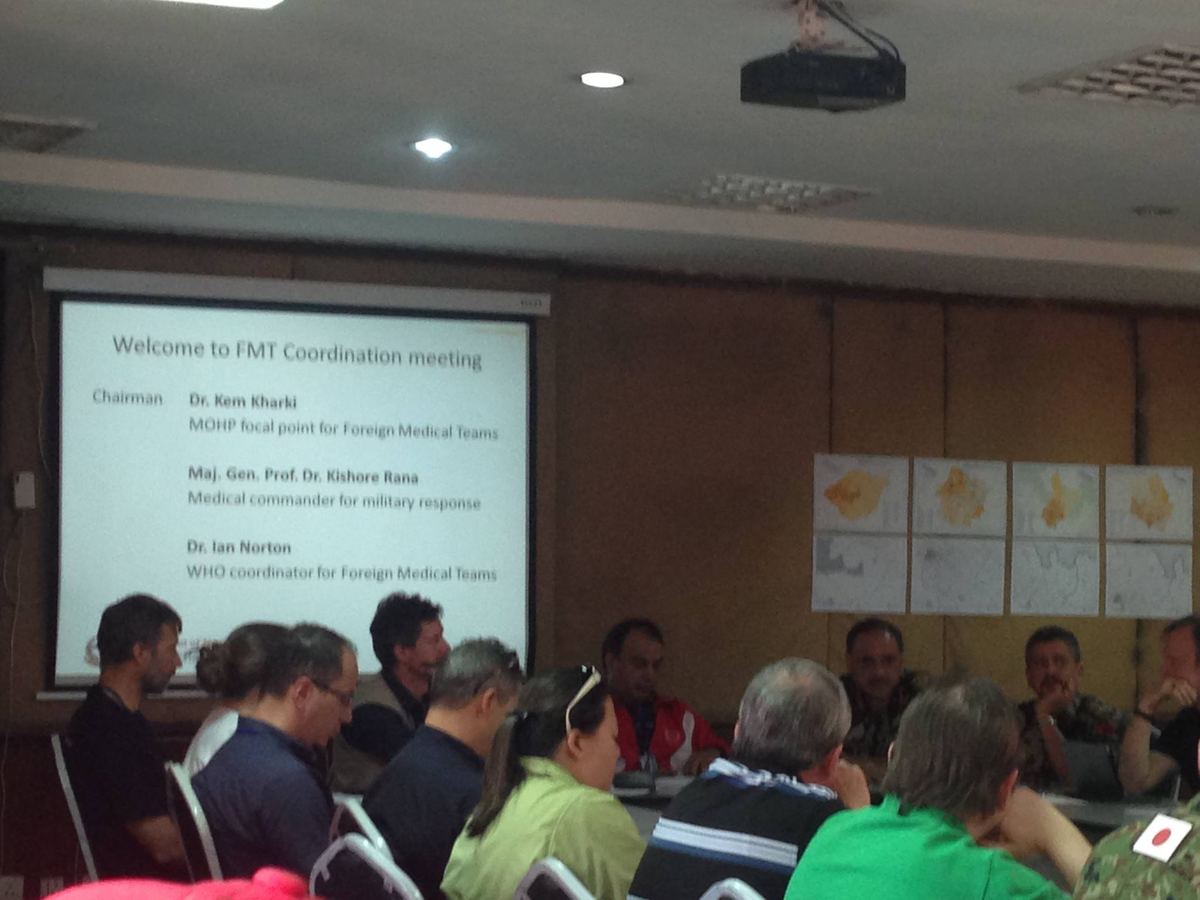 A projected slide reading Welcome to FMT Coordination meeting, listing the chairman and coordinators, above rows of seated delegates.