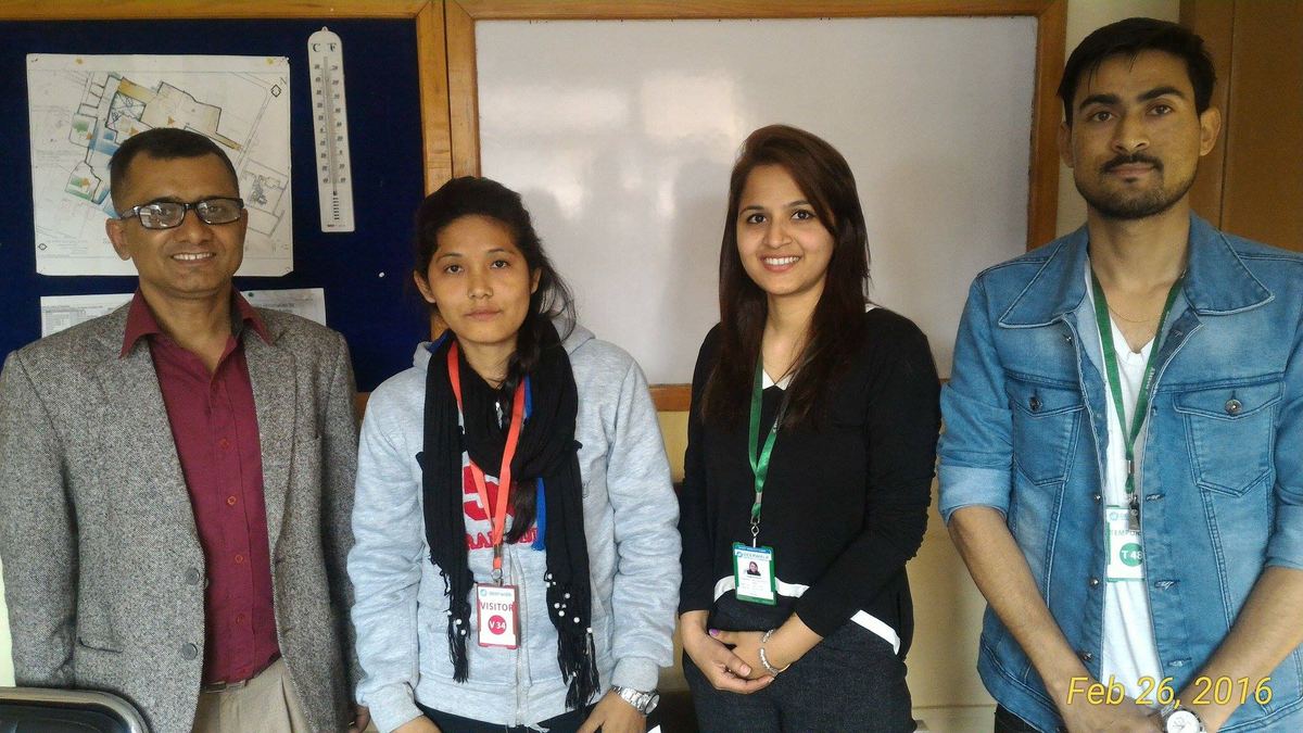 Four people stand in a row in front of an office noticeboard hung with maps and charts.
