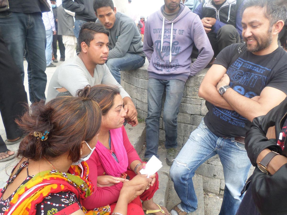 A woman seated on the embankment holds a slip of white paper, with other families and standing volunteers around her.