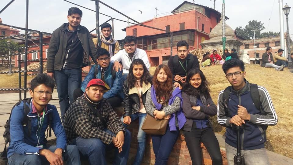 Twelve volunteers stand and crouch together for a group photograph on open ground in front of temple buildings.
