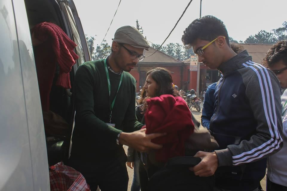 Three volunteers at the open door of a van hand a red bundle of clothing to a woman.