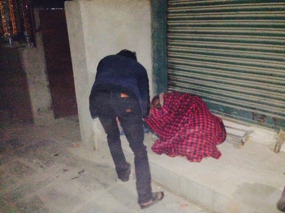 A volunteer walks away from a person wrapped in a red blanket lying on a step in front of closed shutters.